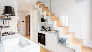 A modern kitchen with a built-in oven, a dining area with a white table, and a staircase with wooden steps. - Apartment 'Melo' with Balcony, Wi-Fi and Air Conditioning (Palermo)
