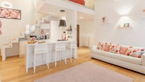 Ein modernes Interieur mit Küche, Essbereich und Wohnzimmer, inklusive Treppe, weißen Möbeln und einem Schlafbereich im oberen Geschoss.