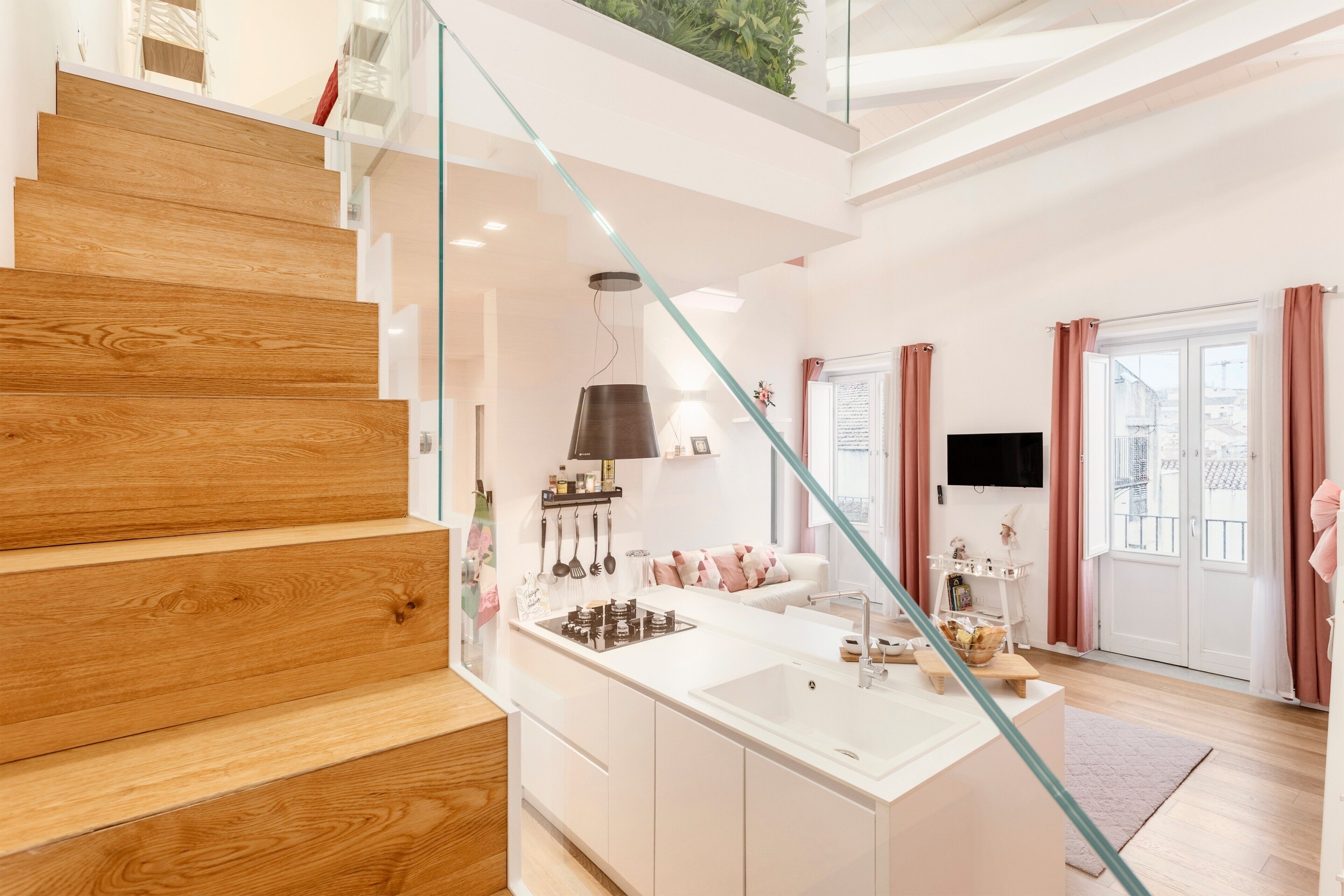 Ein modernes Interieur mit einer Holztreppe, einer Kücheninsel und einem Wohnbereich mit Sofa und Fernseher.