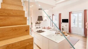 Ein modernes Interieur mit einer Holztreppe, einer Kücheninsel und einem Wohnbereich mit Sofa und Fernseher.