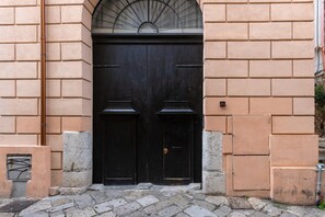 Une porte à deux battants surmontée d’une fenêtre en forme d’éventail, le tout intégré dans un mur en briques de couleur beige.