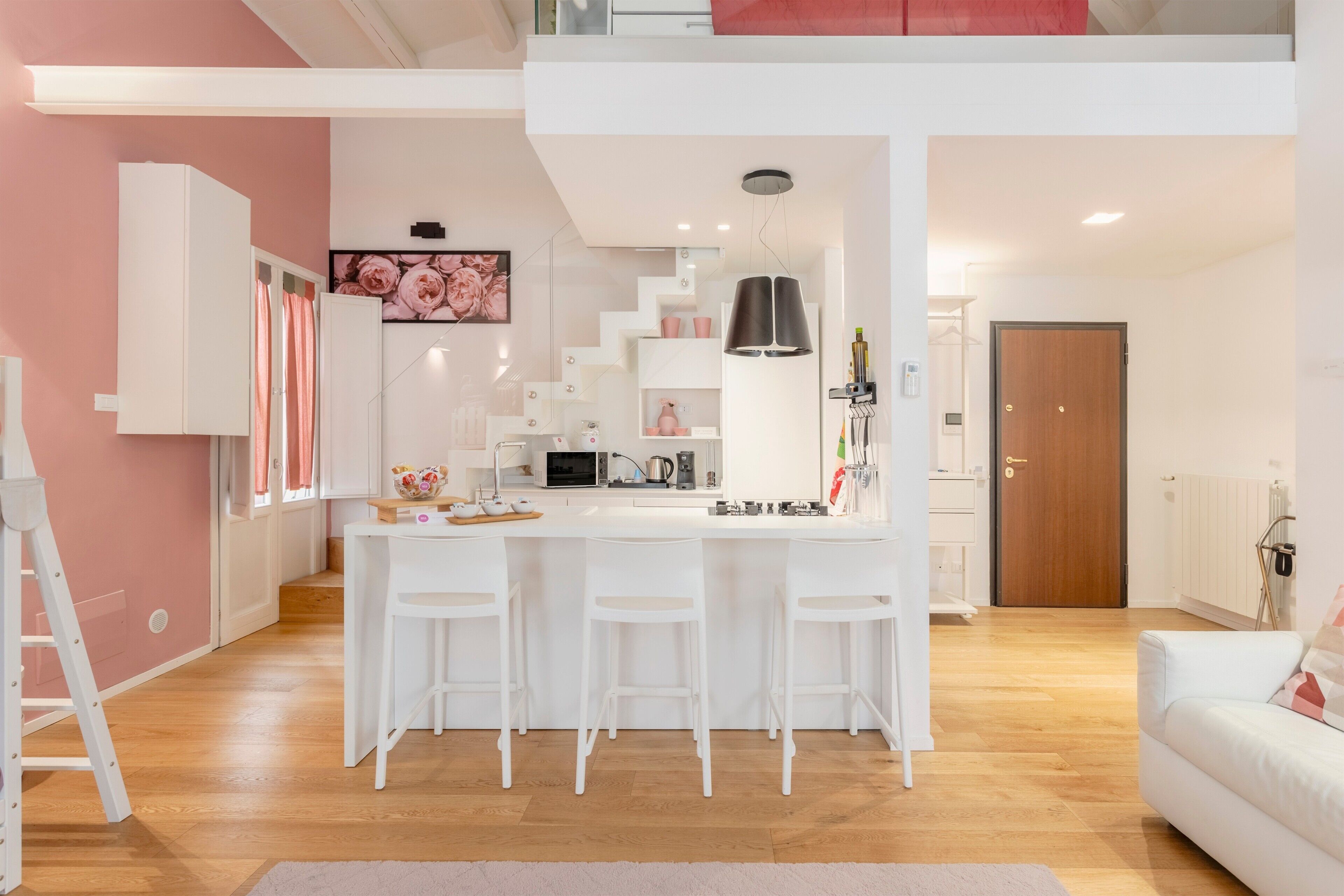 A modern kitchen with a central island, white bar stools, and a loft bedroom above.