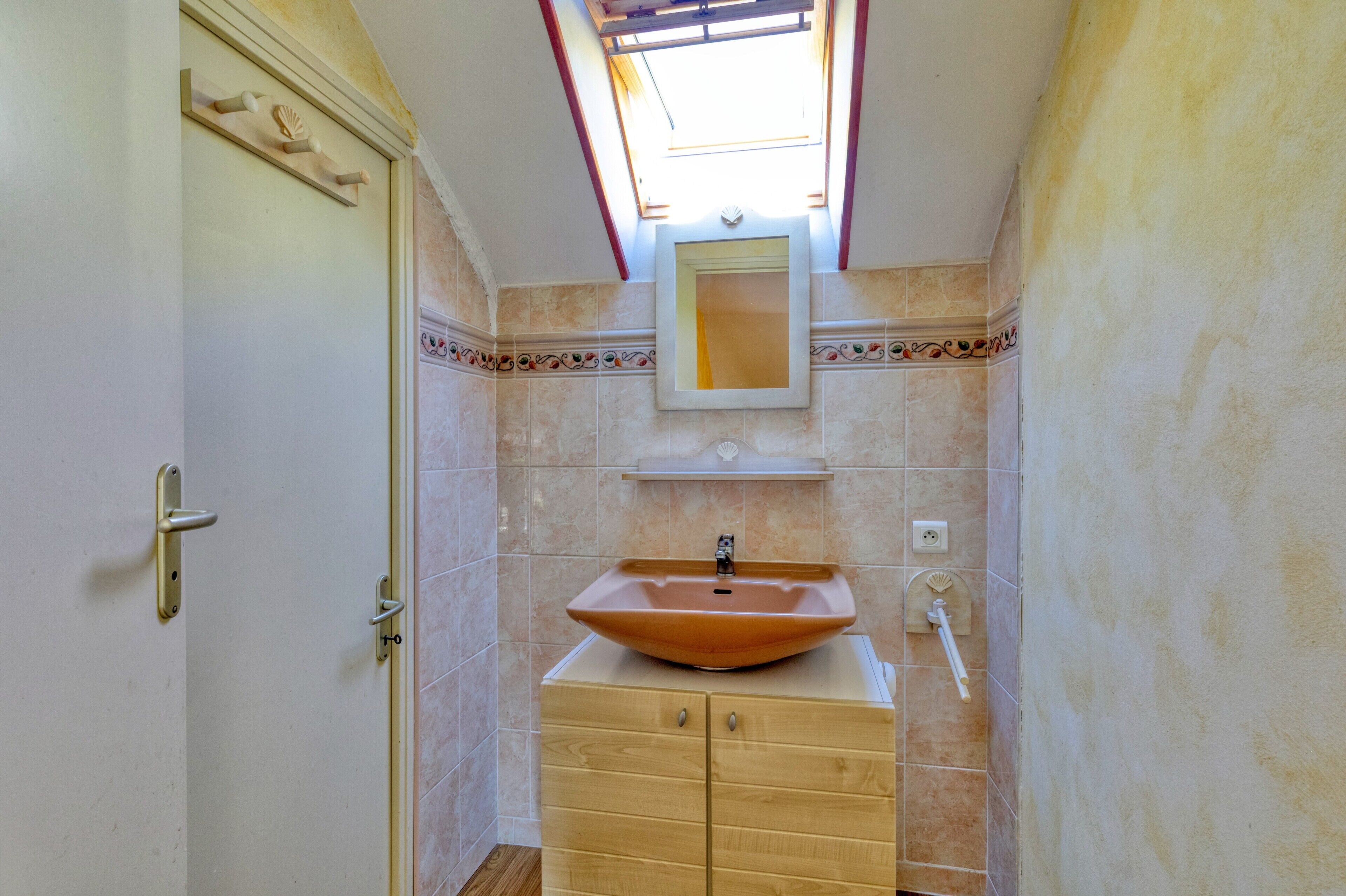 Une salle de bain dotée d’un puits de lumière, d’un grand lavabo sur pied, d’un miroir au-dessus du lavabo et d’un meuble en bois avec des tiroirs.