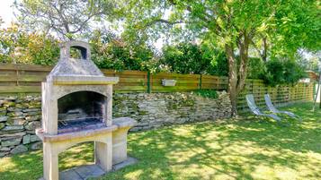 Una griglia in pietra in un giardino sul retro, con un muro in pietra, una recinzione in legno e due poltrone da relax.
