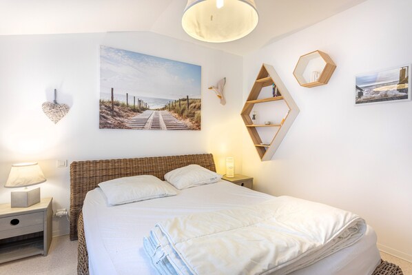 A neatly arranged bedroom with a bed, bedside tables, wall-mounted shelves, and artwork.