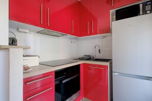 Eine Küche mit roten Schränken, einem weißen Kühlschrank, einem schwarzen Backofen und einer Edelstahl-Spüle.