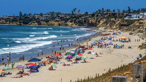 Ein überfüllter Strand mit vielen Sonnenschirmen und Menschen, die das Meer genießen.