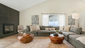 Ein modernes Wohnzimmer mit einem Ecksofa, zwei Holztischen, einem Kamin und abstrakter Wandkunst.
