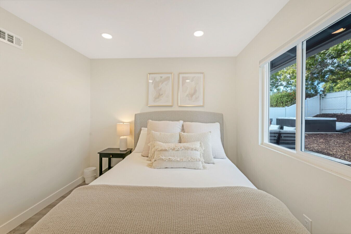 A bedroom with a large bed, a bedside table with a lamp, and a window with a view of the outdoors.
