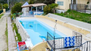 A swimming pool with a covered area, a staircase, and a small building with a tiled roof.