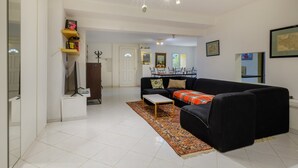 A living room with a black sofa, a coffee table, and a patterned rug. There is a dining area in the background with a table and chairs.