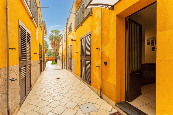 A narrow alleyway with yellow walls and shutters, leading to a door.