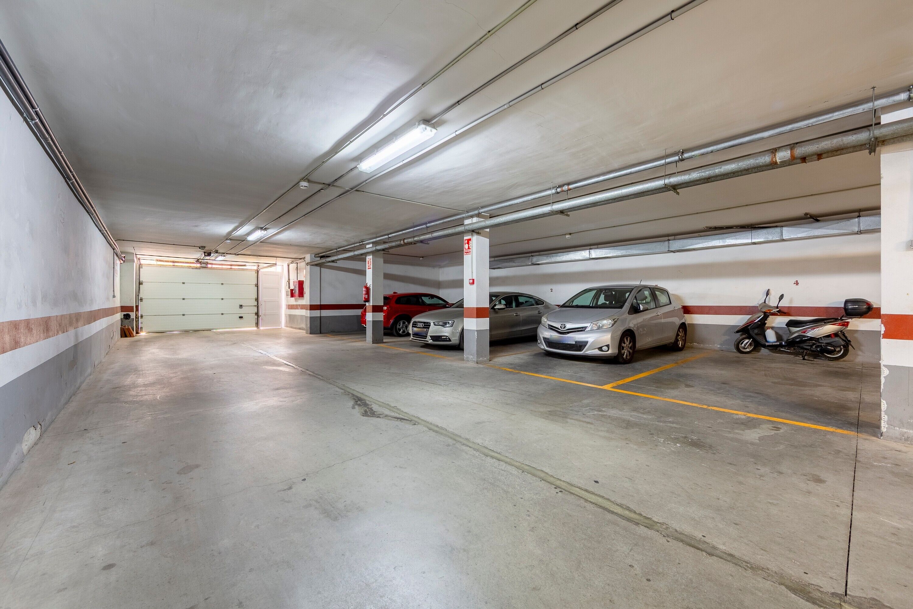A multi-level parking garage with concrete floors, fluorescent lighting, and a fire extinguisher on a pillar.