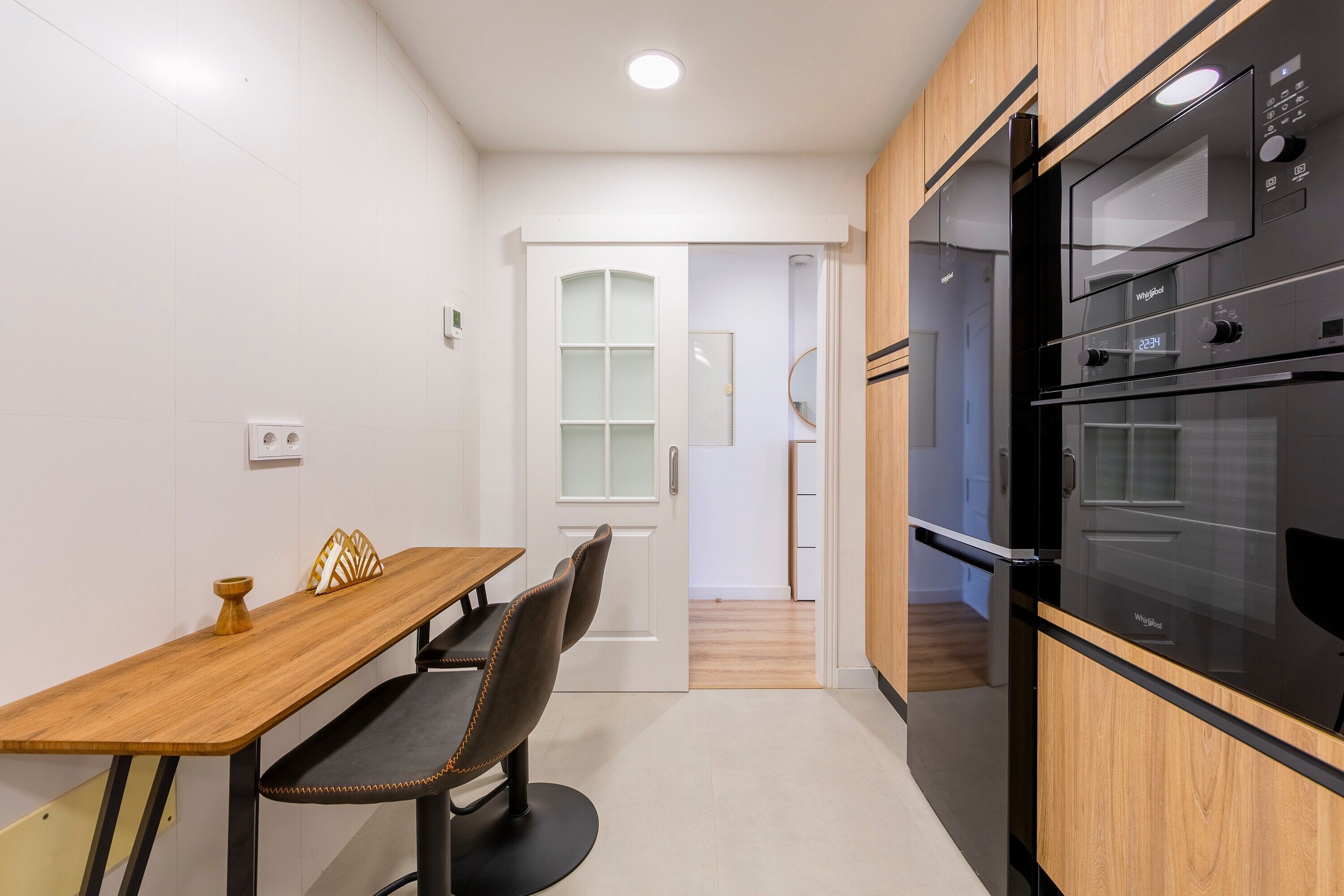 Een moderne keuken met een houten tafel en stoelen, een inbouwoven en een witte deur naar een andere kamer.