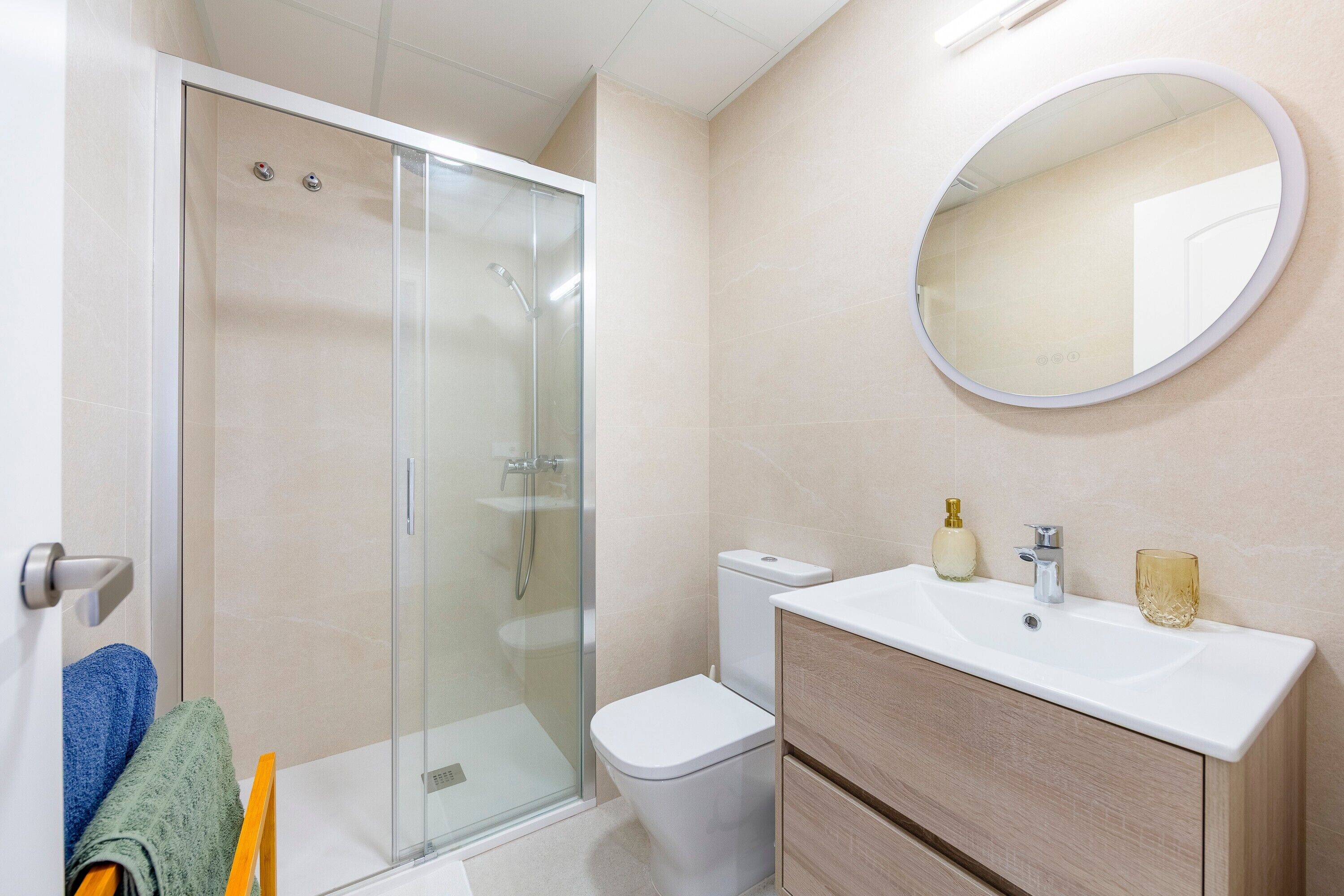 Un baño con ducha envuelta en vidrio, inodoro, lavamanos con espejo y toallero con toallas.