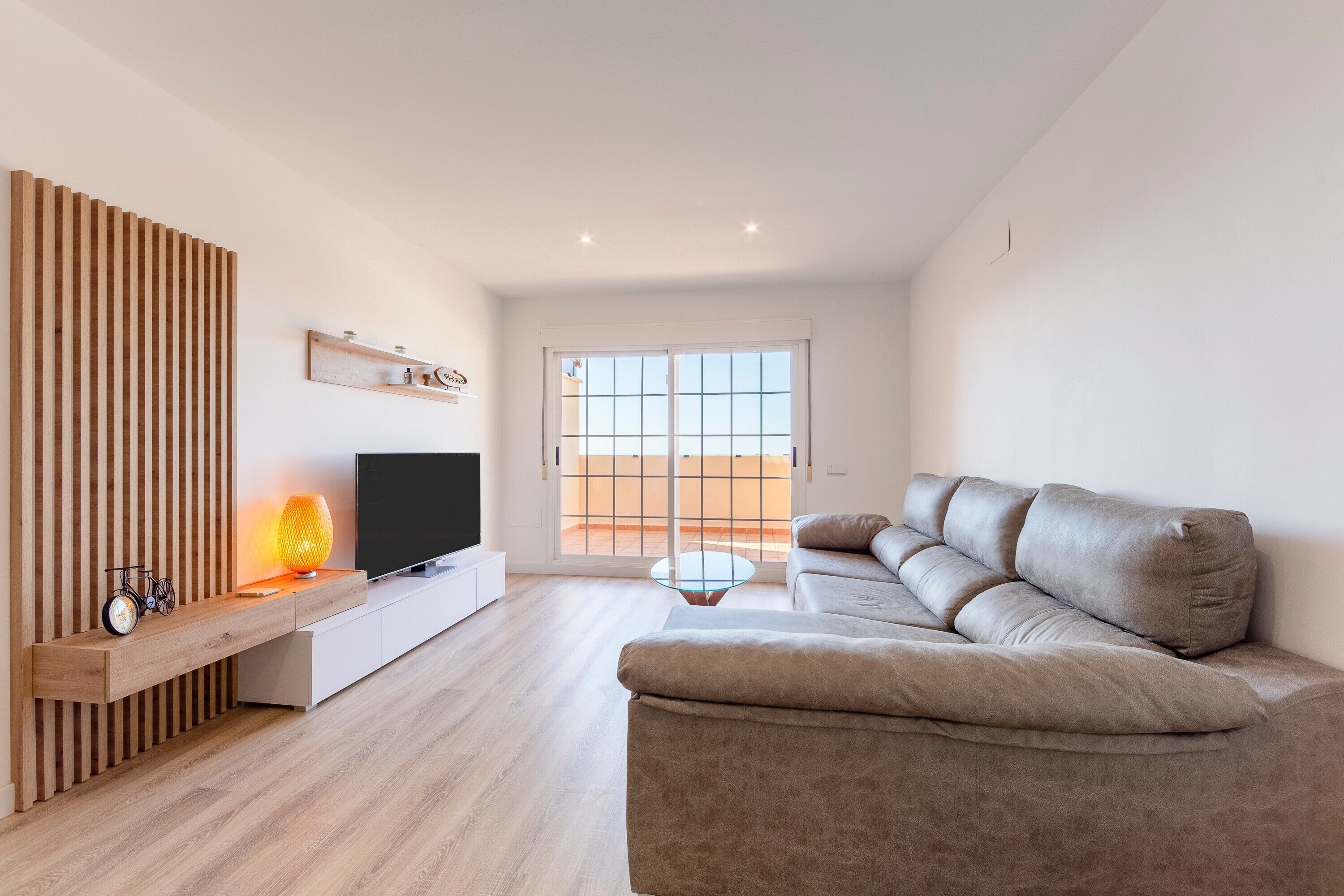 Una sala de estar moderna con un sofá, televisor, pared de listones de madera y una mesa de centro de vidrio.