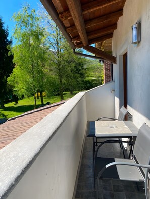 Ein Balkon mit Tisch und Stühlen, einer Holzzieldecke und Blick auf eine grüne Landschaft.
