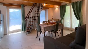 A dining area with a table, chairs, a staircase, and a sofa. - Holiday Home 'Alpi Liguri' with Mountain View, Shared Terrace and Wi-Fi (Peveragno)