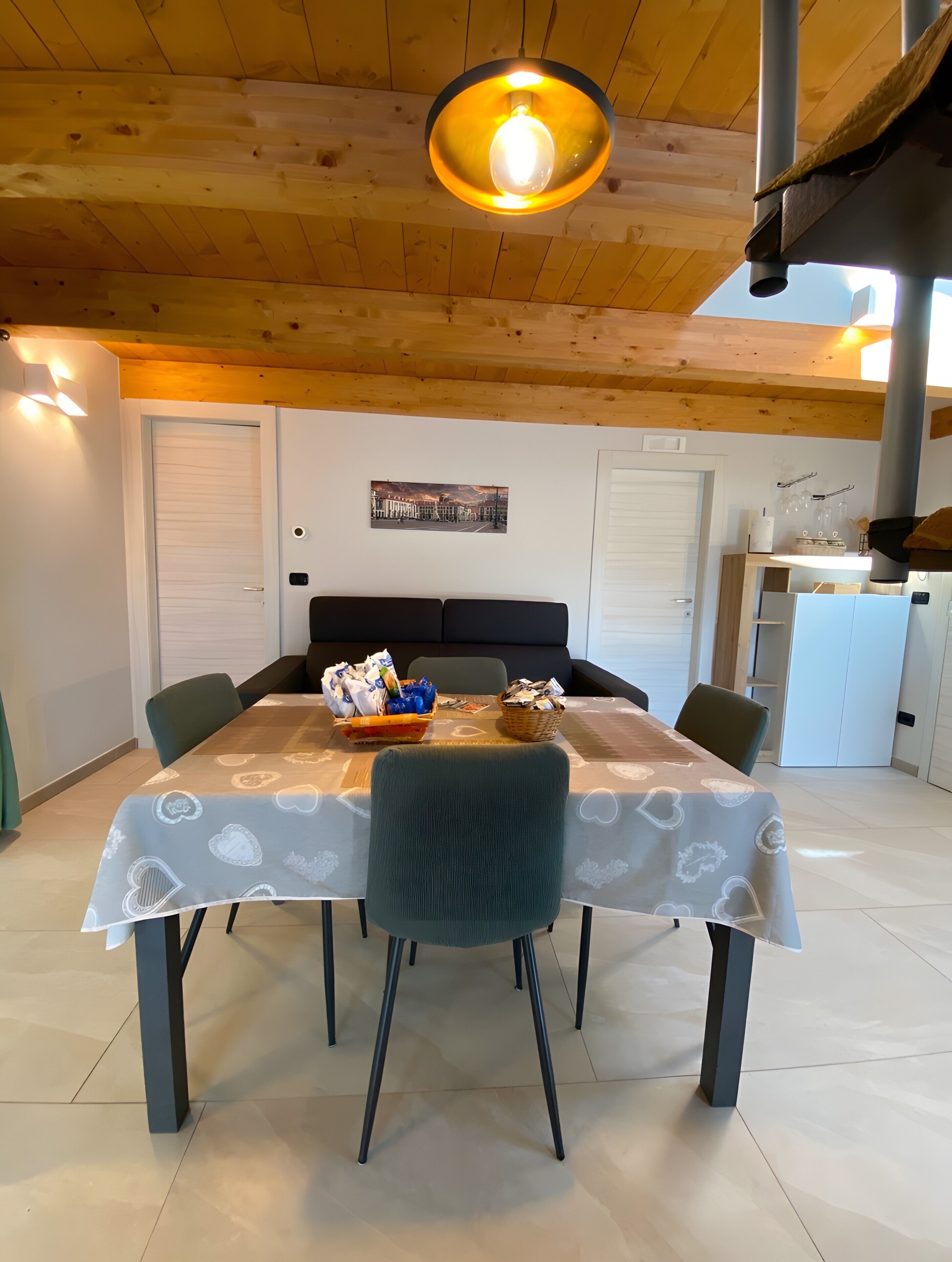 A dining area with a table, chairs, a hanging light fixture, and a bed in the background.