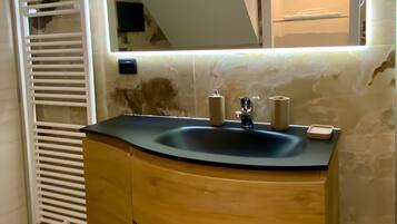 Une salle de bain avec un meuble-lavabo en bois aux lignes courbes, un lavabo avec un miroir et un porte-serviettes.