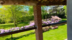 A covered balcony with a brick column, a small potted plant, and a view of a garden with purple flowers and a lawn. - Holiday Home 'Alpi Liguri' with Mountain View, Shared Terrace and Wi-Fi (Peveragno)