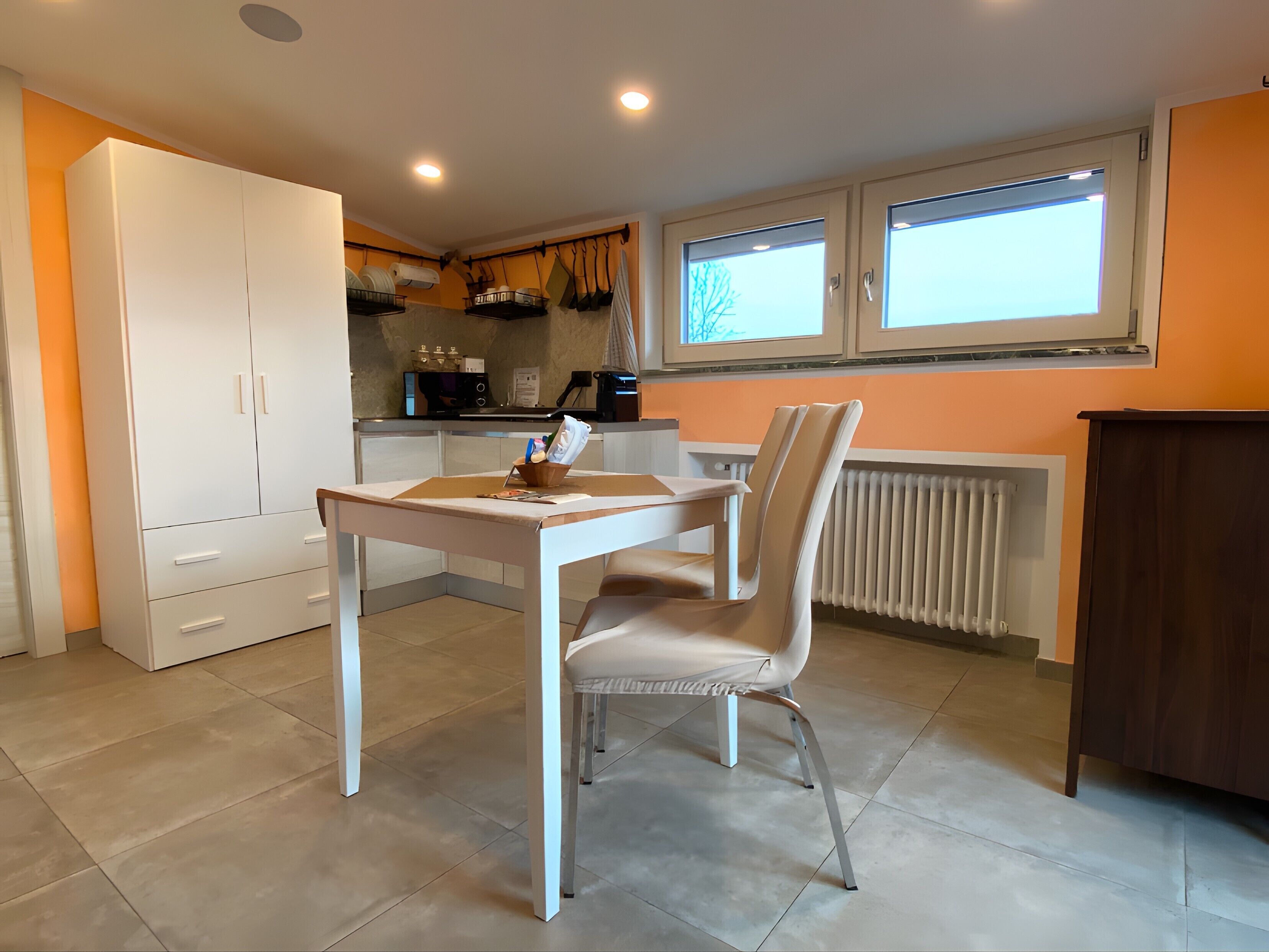 Een keuken met een eettafel en stoelen, een wit kastje en een raam met zonwering.