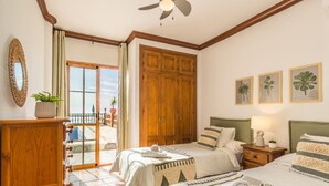 A bedroom with a bed, nightstand, wooden wardrobe, and a balcony with a view. - Villa Vistas Nerja by Ruralidays (Málaga)