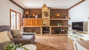 A cozy living room with a fireplace, a sofa, a TV, and a wooden ceiling. - Villa Vistas Nerja by Ruralidays (Málaga)