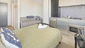 A compact hotel room with a bed, a sofa, a kitchenette, and a door. - Pret-A-Porter (Prahran)