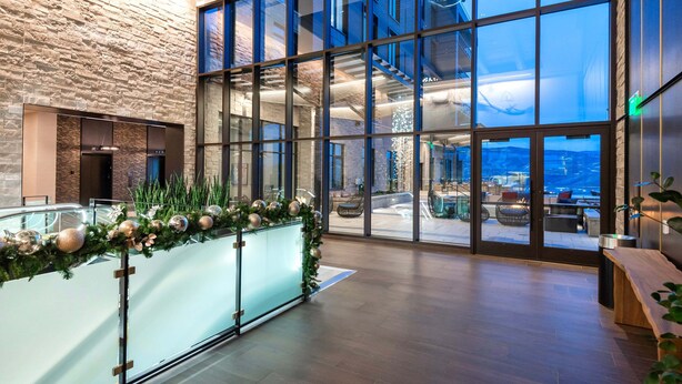 Un hall d’entrée moderne avec un mur en pierre, des portes en verre et une vue sur l’espace extérieur aménagé pour s’asseoir.