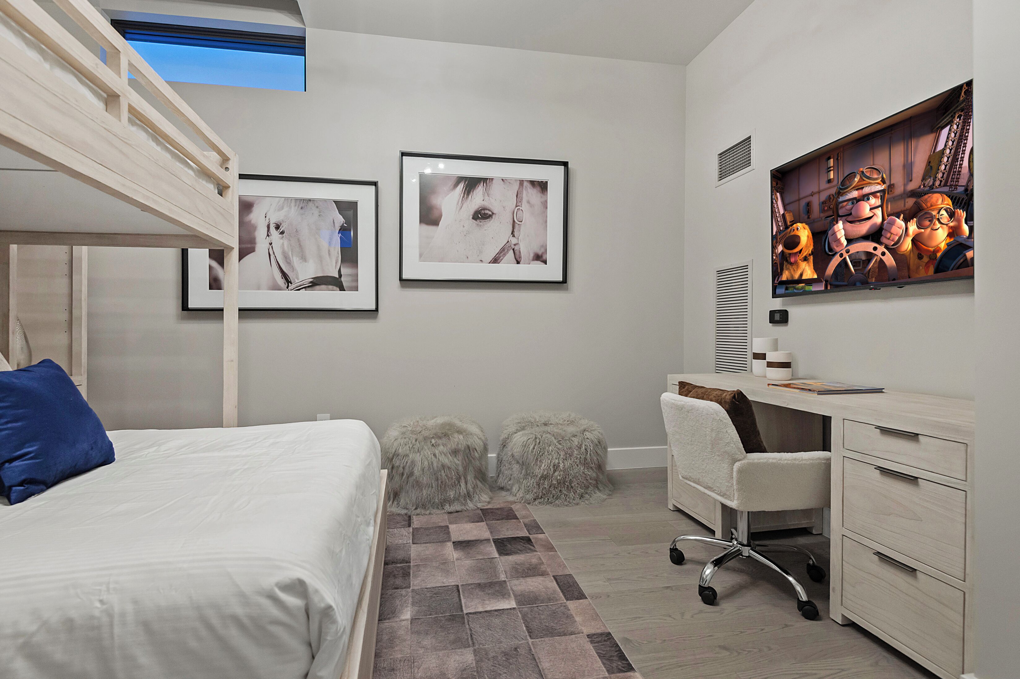 A bedroom with a bunk bed, a desk, a chair, and two fluffy stools.