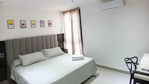 Ein modernes Schlafzimmer mit einem Bett, einem Schreibtisch und einem Stuhl. Es gibt Deckenleuchten und eine Klimaanlage.