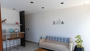 Ein modernes Wohnzimmer mit einer Couch, einem Couchtisch und Sesseln. An der Wand befindet sich ein Regal mit Dekoration und einer Topfpflanze.
