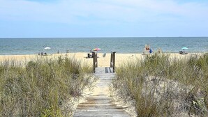 A wooden boardwalk leading to a beach with umbrellas and people. - Private Beach, Hot Tub w/ Ocean Views, Modern 4BR (Bethany Beach)
