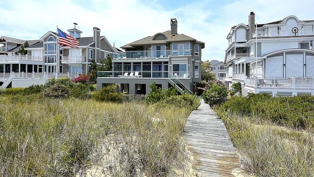 A coastal residential area with houses, a wooden boardwalk, and an American flag. - Private Beach, Hot Tub w/ Ocean Views, Modern 4BR (Bethany Beach)