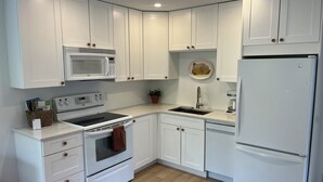 Una cocina moderna con armarios blancos, microondas, estufa, horno, fregadero y refrigerador.