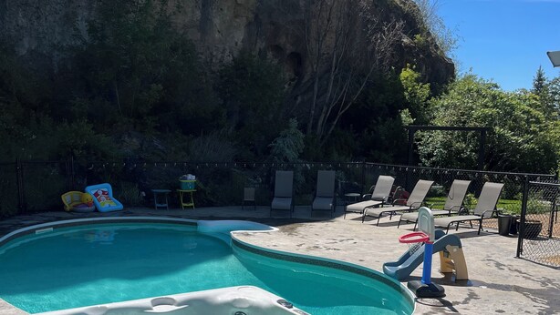 Zona de jacuzzi y piscina con sillones de descanso y un tobogán, rodeada de un risco rocoso y vegetación.