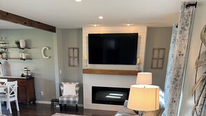 Een moderne woonkamer met een open haard, een flatscreen-tv, een bank, een salontafel en een lamp.
