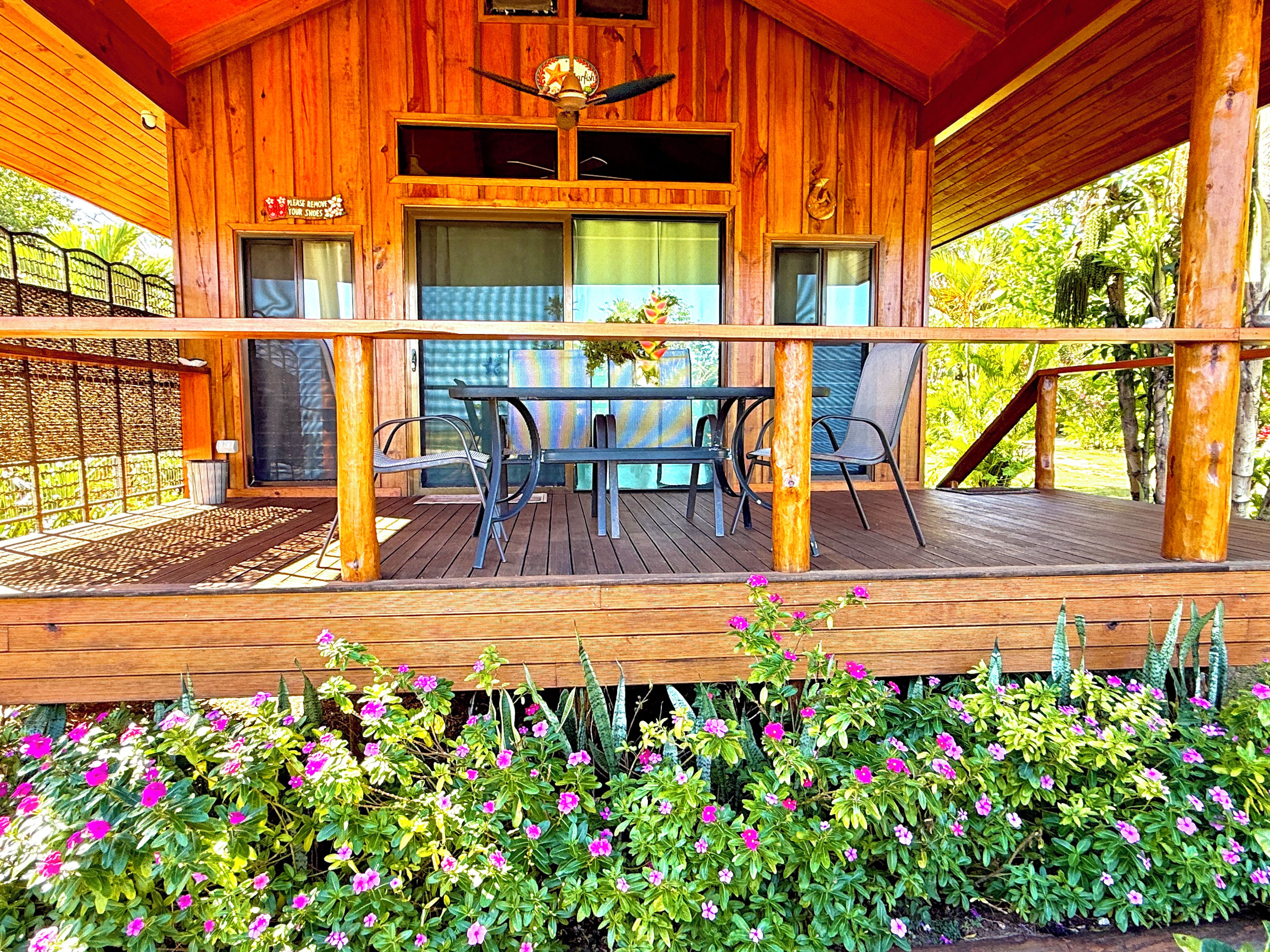 A wooden cabin with a covered porch, a dining table with chairs, and a sign above the windows.