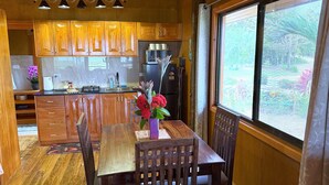 A wooden interior with a dining table, chairs, and a window with a view of greenery.