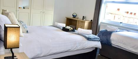 A hotel room with a large bed, a bedside table with a lamp, a small desk with a mirror, and a window with a view of buildings.