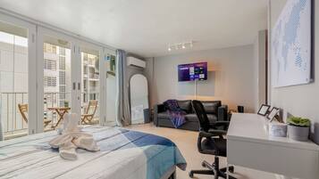 A modern hotel room with a large bed, a desk, a chair, a TV, and a balcony with a view of the city.