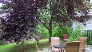 An outdoor patio with wicker furniture, a table, and a tree providing shade. - Huge Manor w Indoor Hot Tub and Pool Table (Bloomington)