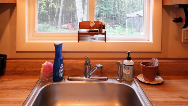 A kitchen with a stainless steel sink, wooden countertop, a window with a view of trees, and a hanging light fixture.