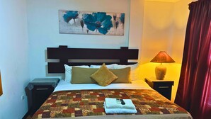Quarto de hotel com cama, mesa de cabeceira, luminária, quadro na parede e janela com cortinas.