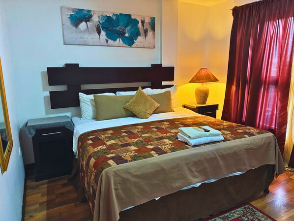 A neatly made bed with a patterned bedspread, a bedside lamp, and a nightstand with a lamp.