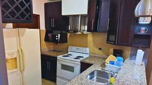Cozinha com armários escuros, geladeira branca, fogão, micro-ondas e bancadas de granito.