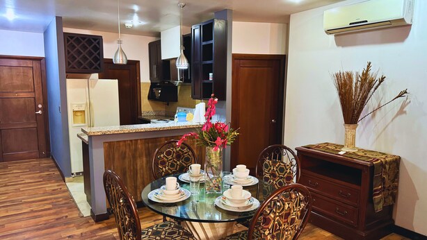 Uma sala de jantar com mesa de vidro, cadeiras estampadas, um vaso com flores e um armário de madeira.
