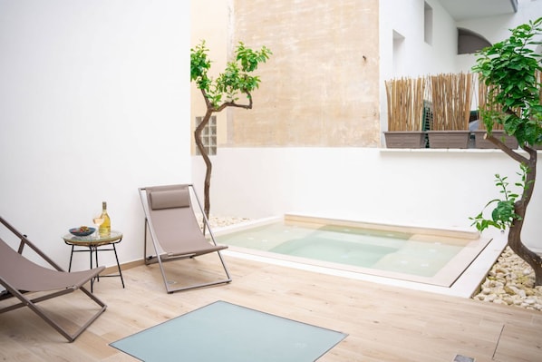 Un espacio exterior pequeño con piscina, dos sillones de descanso, una mesa con una botella y una valla de bambú.