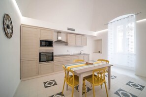 A modern kitchen with built-in appliances, a dining table with yellow chairs, and a patterned floor. - WePuglia - The White Luxury – Apt Nepenthe (Monopoli)